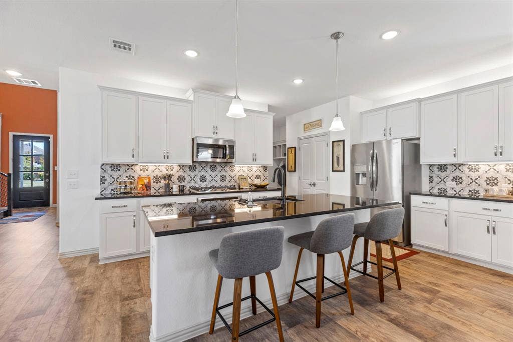 1456 Kit King Drive, Little Elm, TX 75036 Kitchen featuring a large island with dark countertops, white cabinetry, decorative tile backsplash, stainless steel appliances, and wood-finish flooring