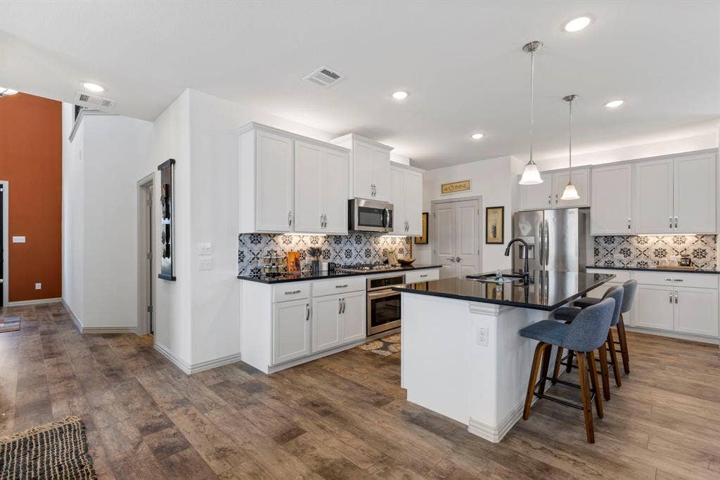 1456 Kit King Drive, Little Elm, TX 75036 Kitchen featuring wood-finish flooring, white cabinetry, black countertops, and a patterned tile backsplash