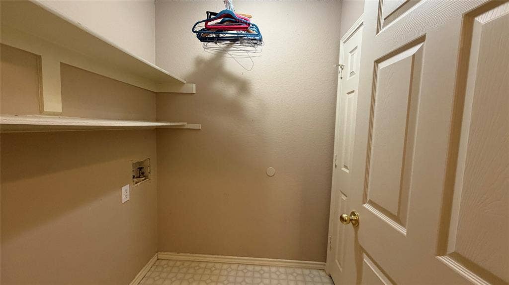 2718 High Pointe Boulevard, McKinney, TX 75071 Laundry area with built-in shelving, patterned floor tiles, and a panel door with a brass-finish knob