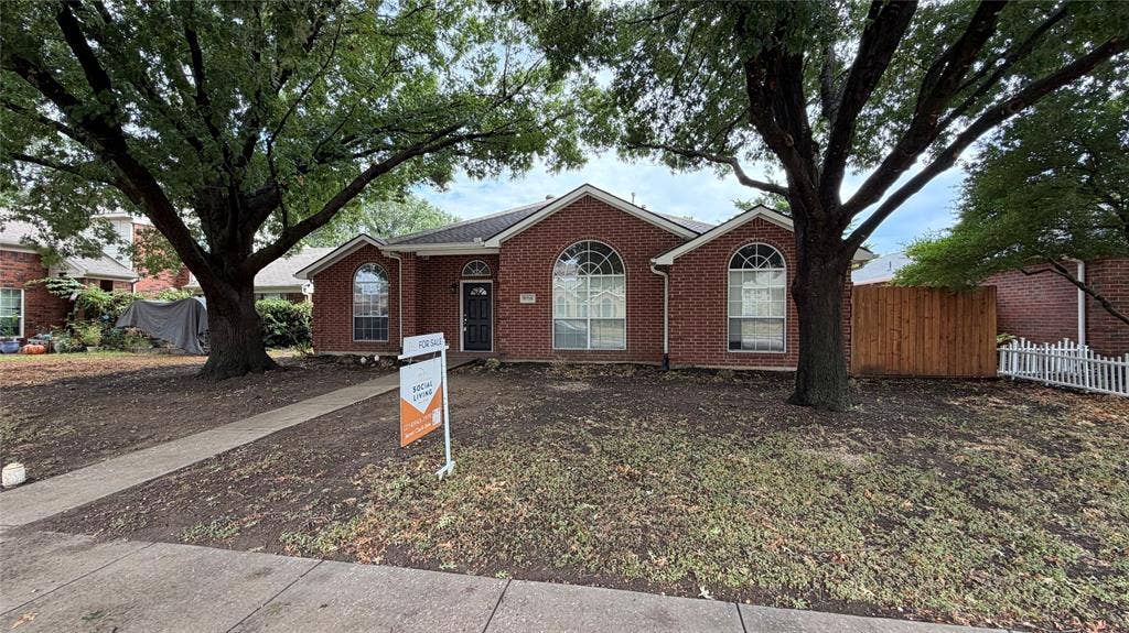 2718 High Pointe Boulevard, McKinney, TX 75071 Brick exterior with arched windows, mature shade trees, a concrete walkway, and a partial wood fence