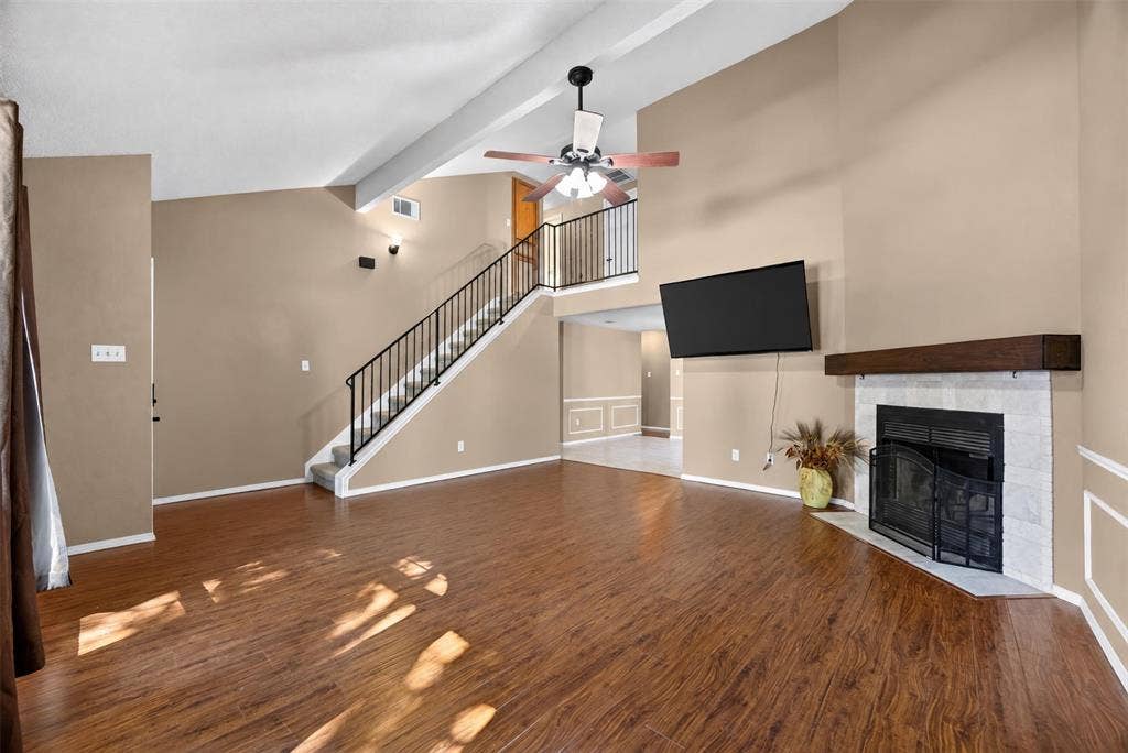 203 Briarglen Drive, Cedar Hill, TX 75104 Vaulted ceiling with a ceiling fan, wood-finish flooring, fireplace with a tile surround and wood mantel, and a staircase with a black metal railing