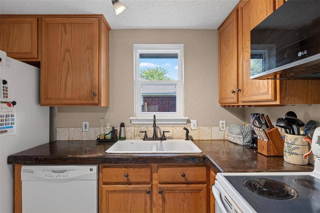 203 Briarglen Drive, Cedar Hill, TX 75104 Warm wood cabinetry with dark countertops, a white undermount sink with a dark faucet, and a tiled backsplash