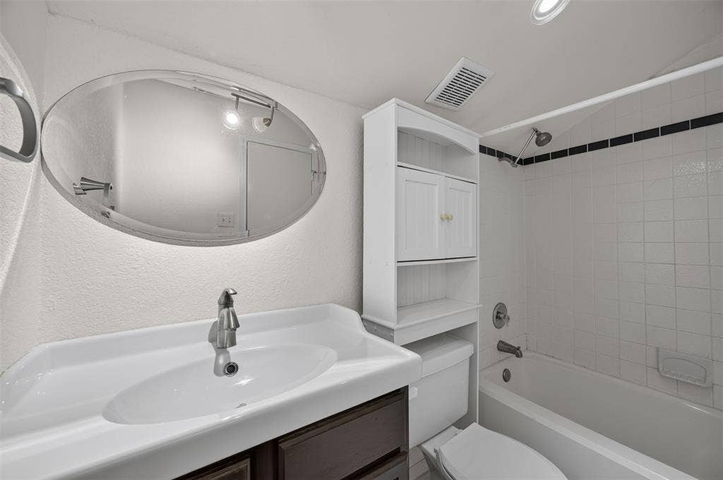 203 Briarglen Drive, Cedar Hill, TX 75104 Bathroom featuring a white ceramic vanity sink, a wall-mounted oval mirror, a white built-in storage cabinet, a white bathtub with tile surround, and a chrome shower fixture