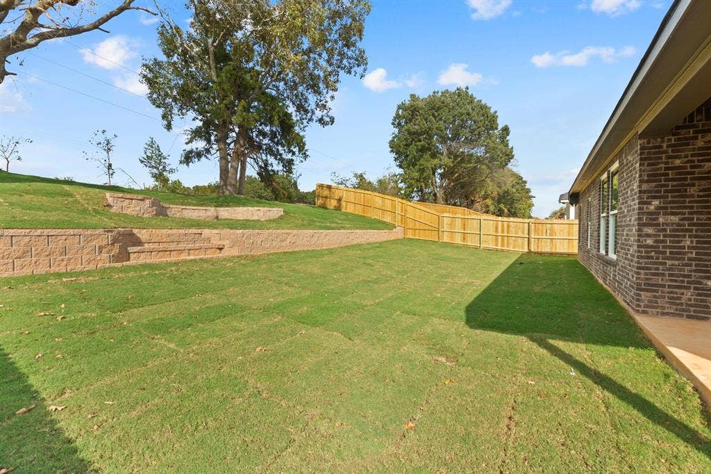 16514 Crossing Circle, Lindale, TX 75771 Expansive backyard with a level lawn, terraced retaining walls, and a wood privacy fence