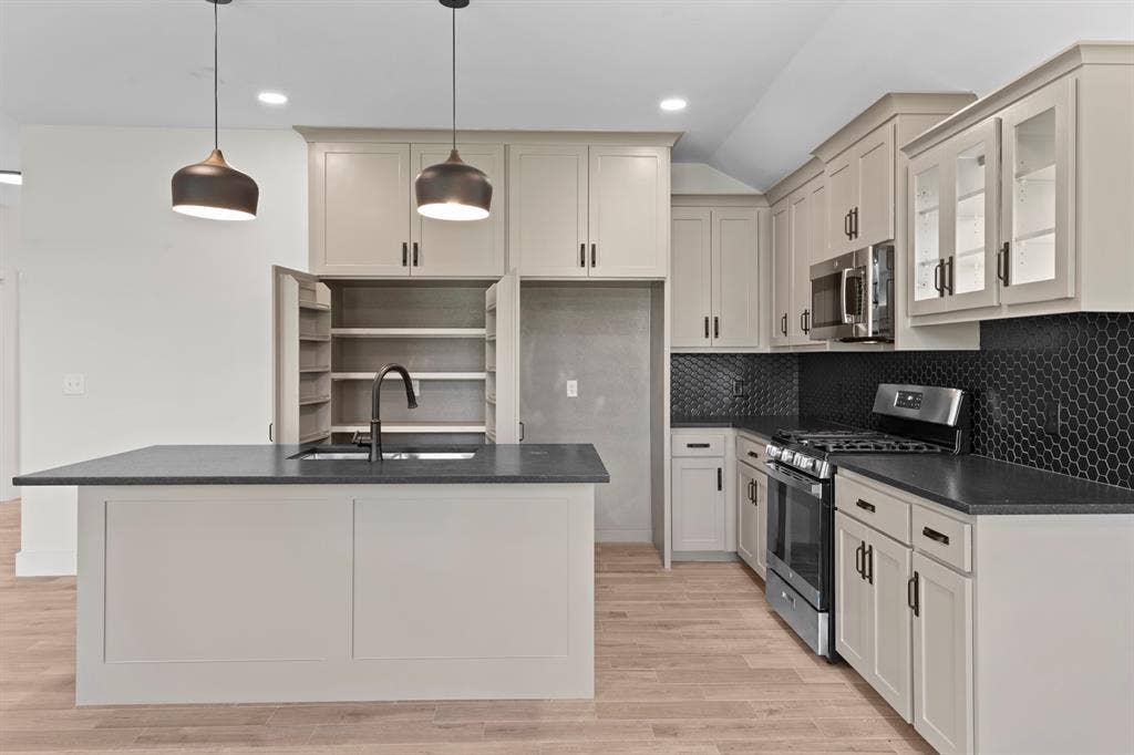 16514 Crossing Circle, Lindale, TX 75771 Kitchen featuring a central island with an undermount sink, pendant lighting, built-in pantry cabinetry, black hexagonal tile backsplash, and stainless steel appliances