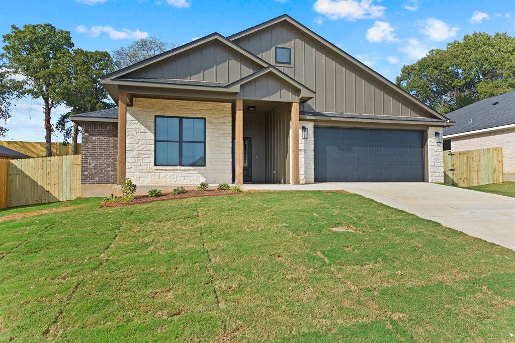 16514 Crossing Circle, Lindale, TX 75771 Stone and vertical siding exterior with wood-wrapped columns, a dark garage door, and a concrete driveway