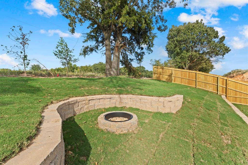16514 Crossing Circle, Lindale, TX 75771 Expansive backyard featuring a manicured lawn, a stone retaining wall, and a built-in fire pit