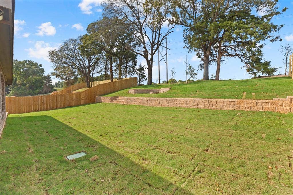 16514 Crossing Circle, Lindale, TX 75771 Expansive grassy yard featuring a new privacy fence and multiple retaining walls with integrated steps