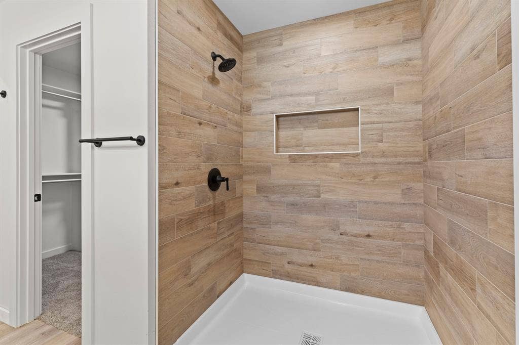 16514 Crossing Circle, Lindale, TX 75771 Shower featuring wood-finish tile walls, a built-in shower niche, and matte black fixtures