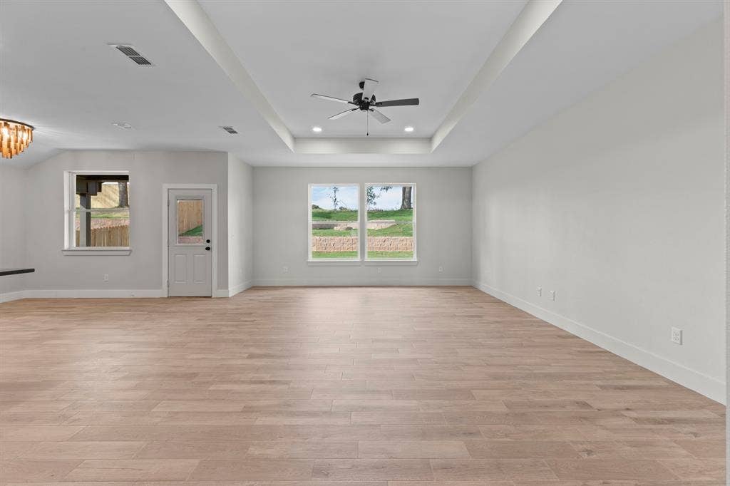 16514 Crossing Circle, Lindale, TX 75771 Spacious interior with wood-finish flooring, white walls, and a tray ceiling featuring a ceiling fan