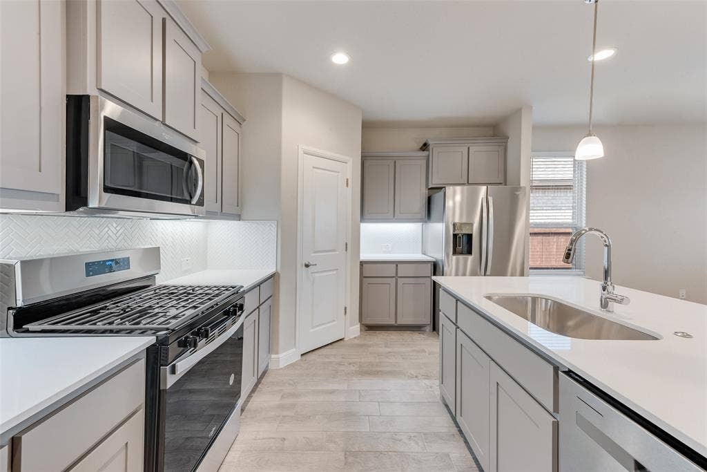Kitchen featuring stainless steel appliances, hanging light fixtures, sink, and gray cabinets