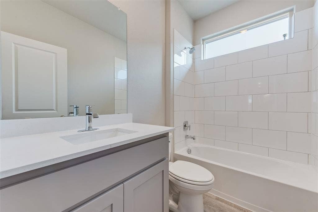 Full bathroom with hardwood / wood-style flooring, tiled shower / bath, vanity, and toilet