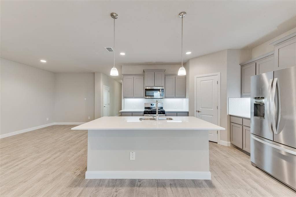 Kitchen with stainless steel appliances, a kitchen island with sink, gray cabinetry, and decorative light fixtures