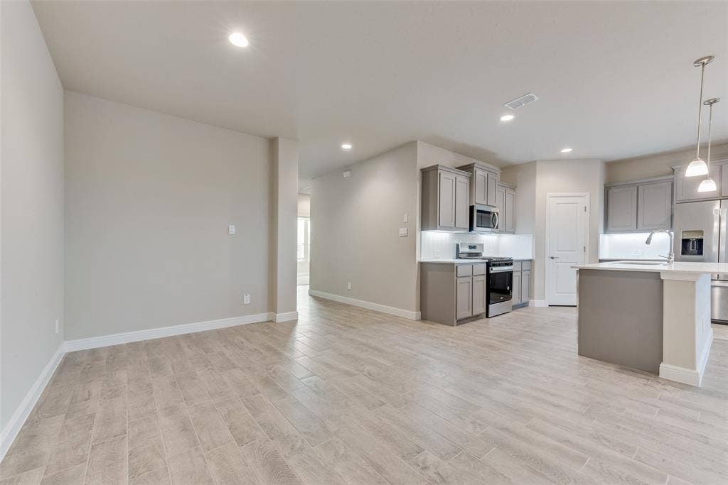 Kitchen with pendant lighting, sink, gray cabinets, light hardwood / wood-style flooring, and appliances with stainless steel finishes