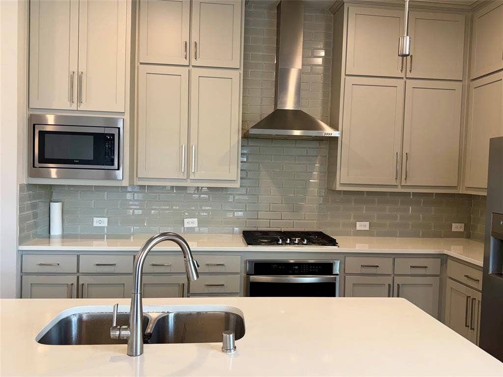 1196 Putnam Drive, Frisco, TX 75036 Kitchen featuring light gray cabinetry, white countertops, glass subway tile backsplash, stainless steel appliances, and a kitchen island with an undermount sink