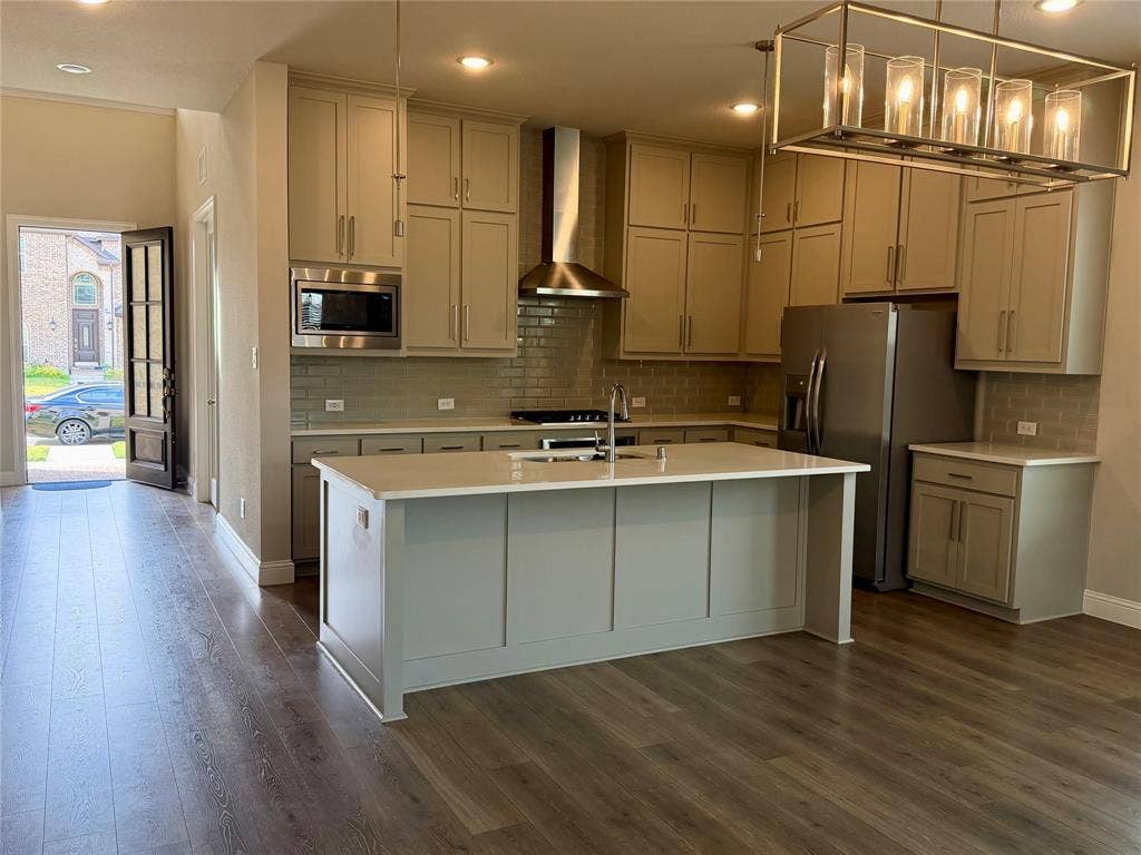 1196 Putnam Drive, Frisco, TX 75036 Modern kitchen featuring wood-finish flooring, a large central island with a light-colored countertop, abundant cabinetry, and stainless steel appliances