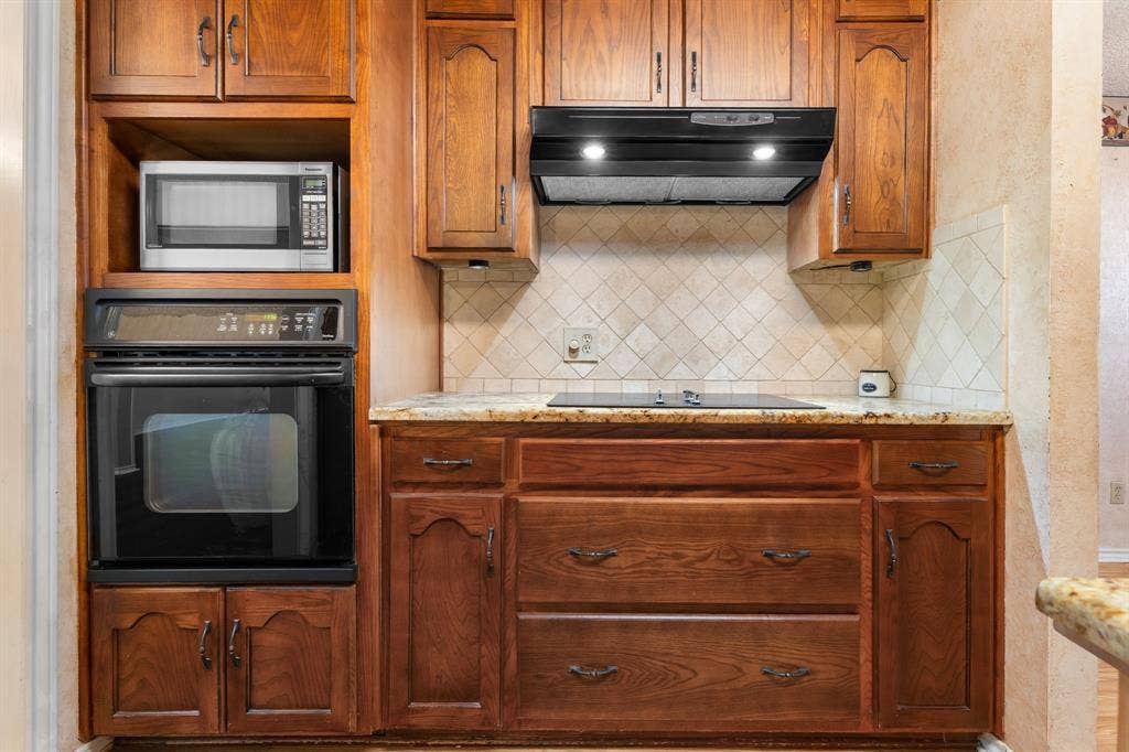 544 Jason Street, Robinson, TX 76706 Rich wood cabinetry with dark bronze hardware, built-in oven, built-in microwave, integrated cooktop, and speckled stone countertops