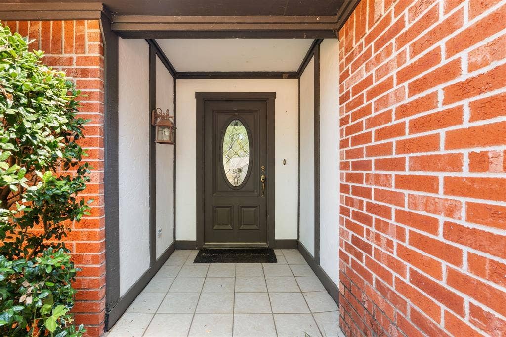 544 Jason Street, Robinson, TX 76706 Brick exterior walls with white mortar, recessed entry, dark wood-finish entry door with oval glass insert, exterior wall light fixture, and light-colored tile flooring