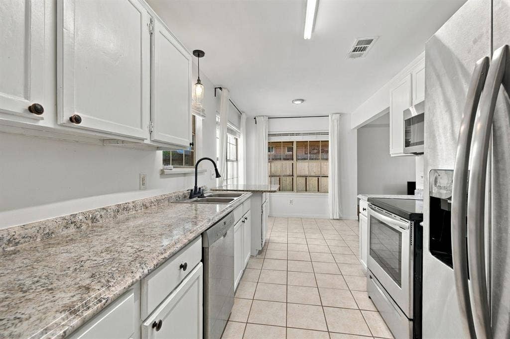 1015 Shelly Drive, Keene, TX 76031 White cabinetry, speckled countertops, stainless steel appliances, tile flooring, and a double basin sink with a gooseneck faucet