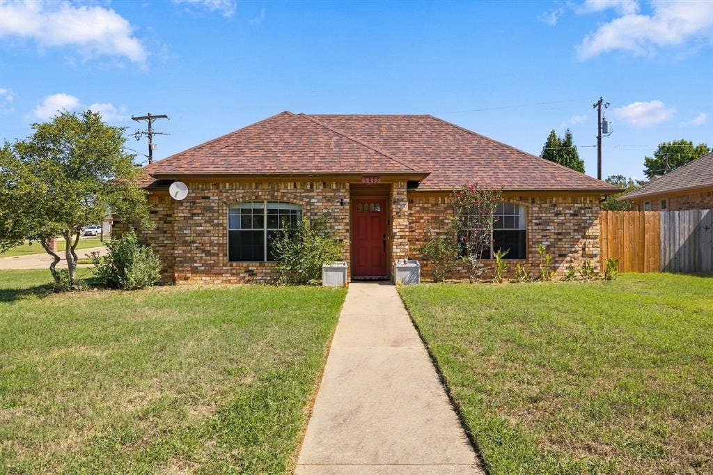 1015 Shelly Drive, Keene, TX 76031 Brick exterior residence featuring a red entry door, gabled roof, and a concrete pathway