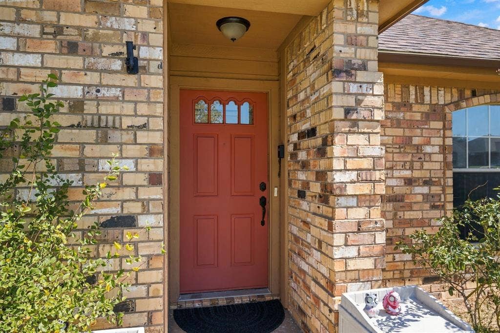 1015 Shelly Drive, Keene, TX 76031 Brick exterior with a vibrant red entry door featuring decorative glass lites, a shingled roof, and an arched window