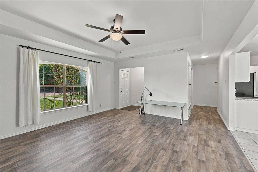 1015 Shelly Drive, Keene, TX 76031 Tray ceiling with a ceiling fan light fixture, wood-finish flooring, a large arched window, and a paneled entry door
