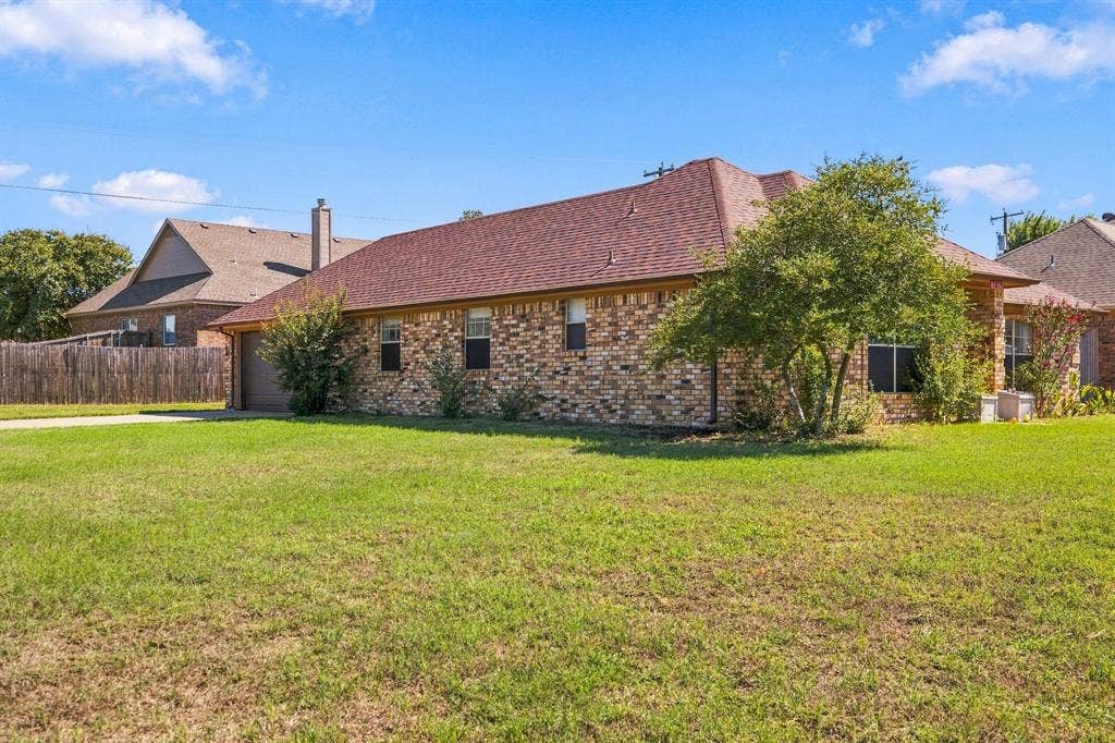 1015 Shelly Drive, Keene, TX 76031 Brick exterior, red shingle roof, attached garage, established landscaping, and a manicured lawn