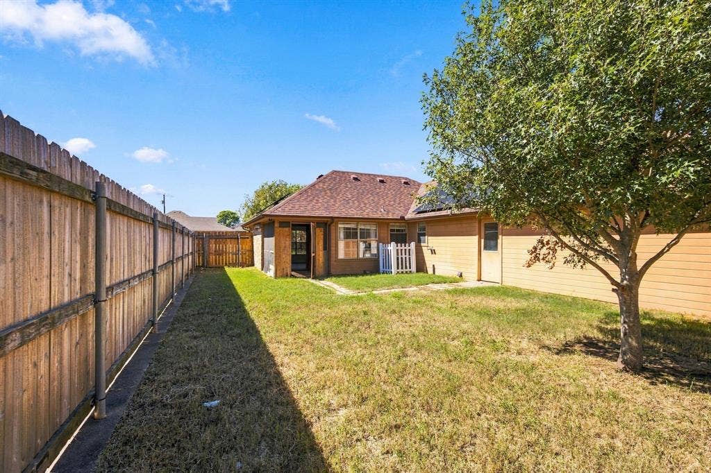 1015 Shelly Drive, Keene, TX 76031 Private backyard featuring a full wood fence, mature tree, and a secondary side door