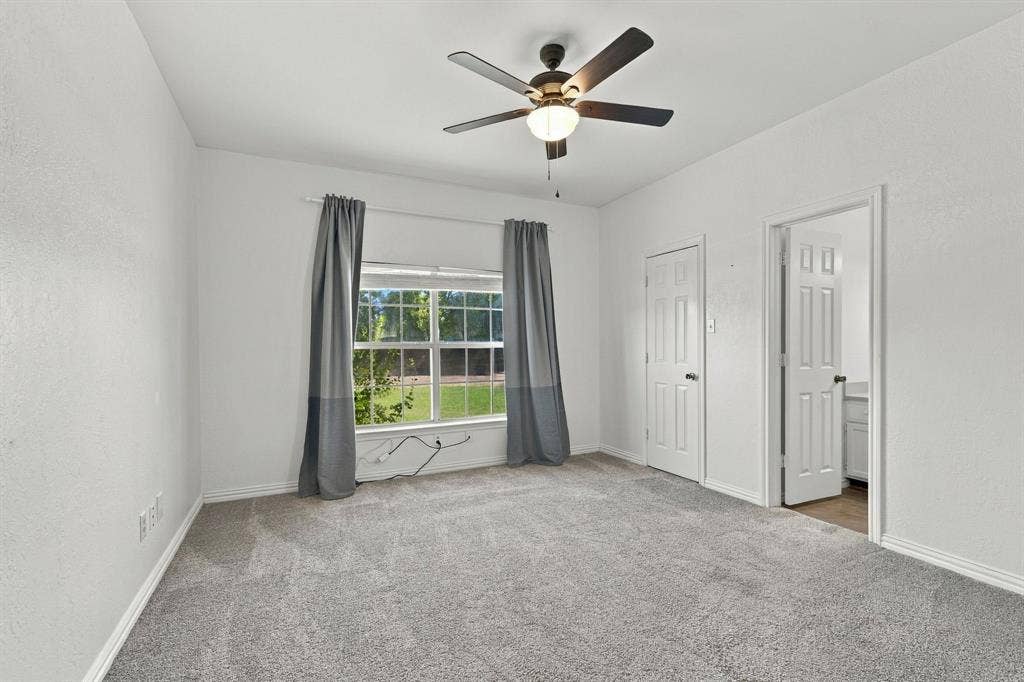 1015 Shelly Drive, Keene, TX 76031 Expansive room with neutral carpeting, a ceiling fan with integrated lighting, and a large window