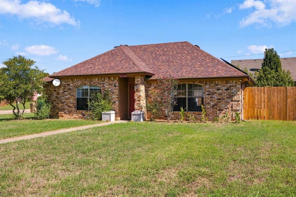 1015 Shelly Drive, Keene, TX 76031 Brick facade residence featuring a shingle roof, arched windows, and a wood privacy fence