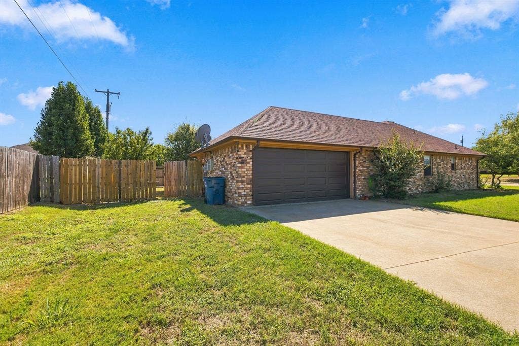 1015 Shelly Drive, Keene, TX 76031 Brick exterior with an attached garage, paved driveway, and a fenced backyard