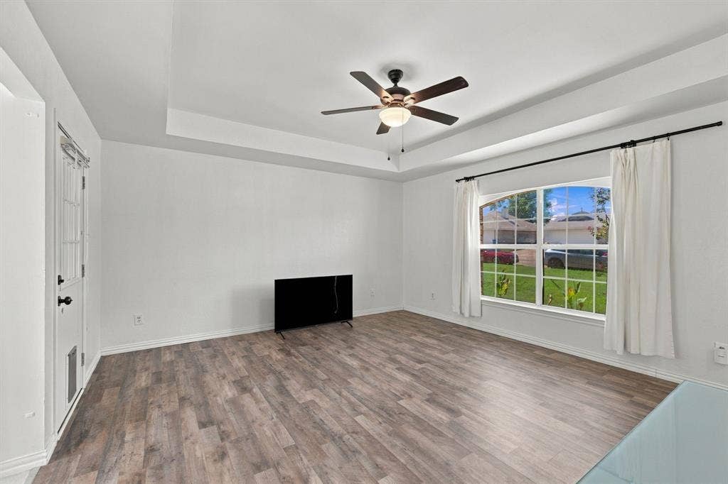 1015 Shelly Drive, Keene, TX 76031 Spacious room featuring wood-finish flooring, a tray ceiling, and a ceiling fan with light fixture