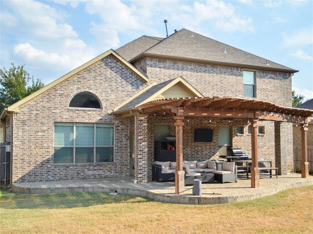 Brick exterior with a large patio featuring a wooden pergola, an arched window, and a shingle roof