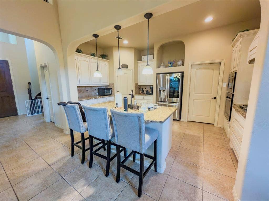Kitchen featuring an expansive island with a light-toned countertop, white cabinetry, integrated stainless steel refrigerator, and tiled flooring