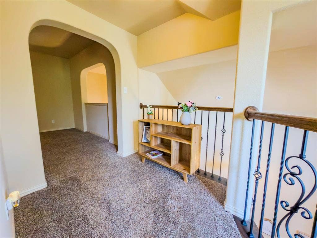 Arched entryway, carpeted flooring, black wrought iron railing, and wooden handrail