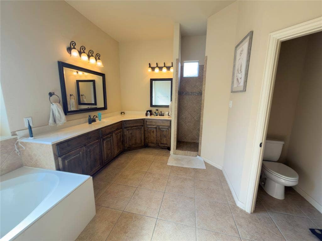 Spacious bathroom featuring an integrated soaking tub, dual vanities with dark wood cabinetry, a tiled walk-in shower, and tile flooring