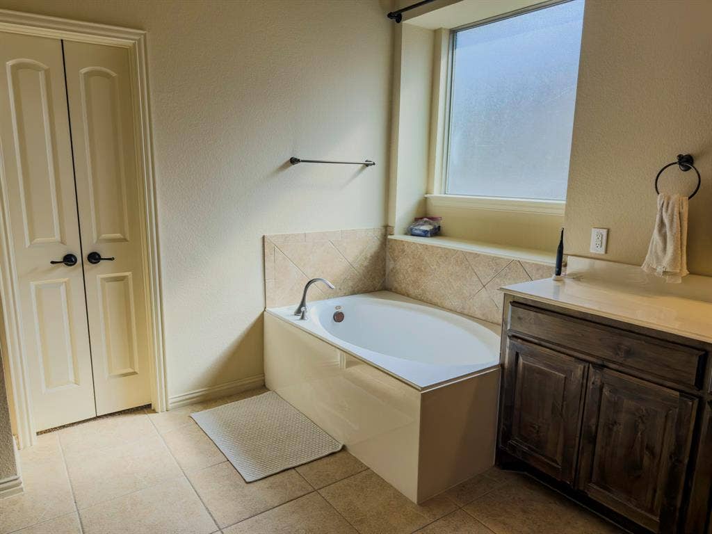 Built-in soaking tub with tile surround, wood-finish vanity with countertop, and double-panel doors
