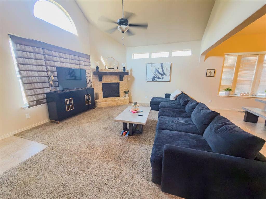 Vaulted ceilings with a ceiling fan, stone-clad fireplace, arched window, and carpet flooring