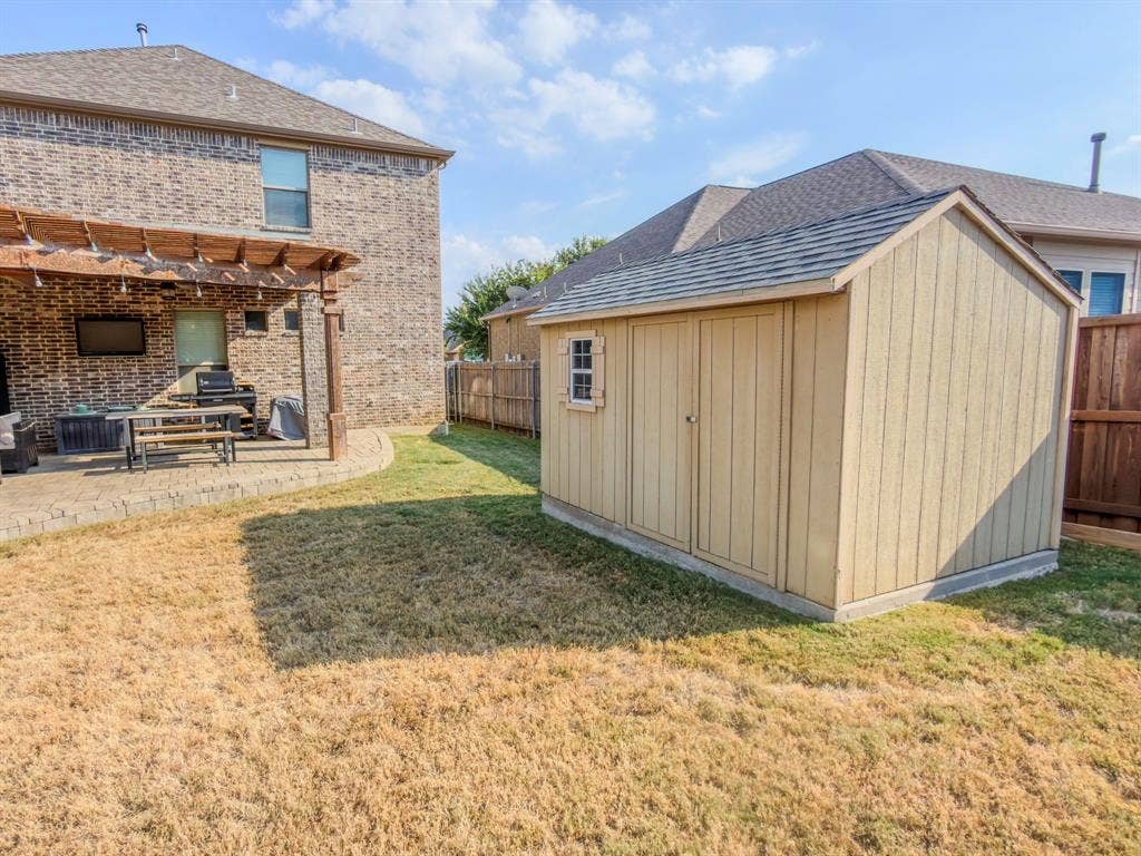 Outdoor patio with a wood pergola, brick exterior, and a detached storage shed