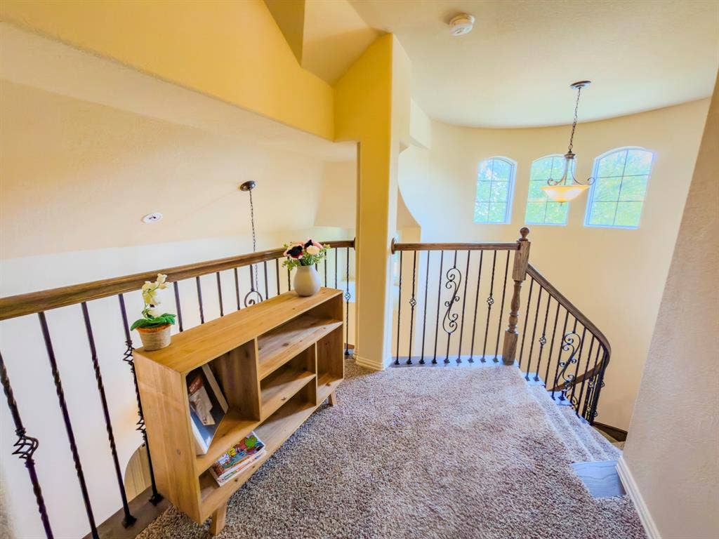 Loft area with carpet flooring, wrought iron railing, arched windows, and a hanging light fixture
