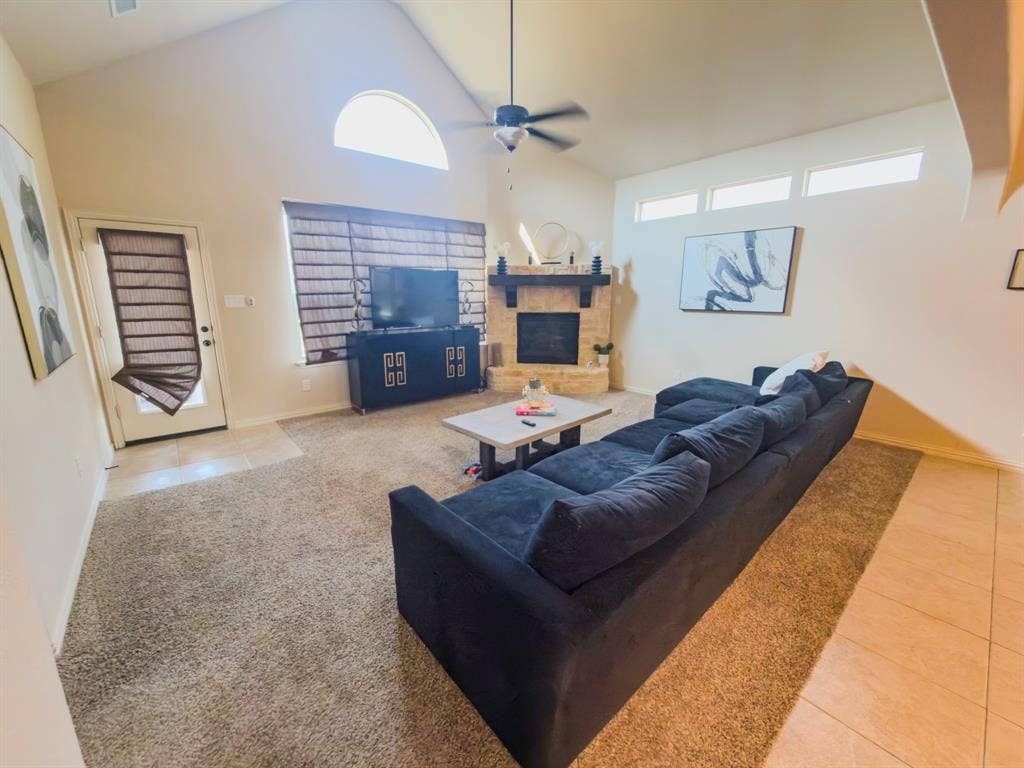 Vaulted ceiling, stone fireplace with mantel, ceiling fan, transom windows, and tile flooring