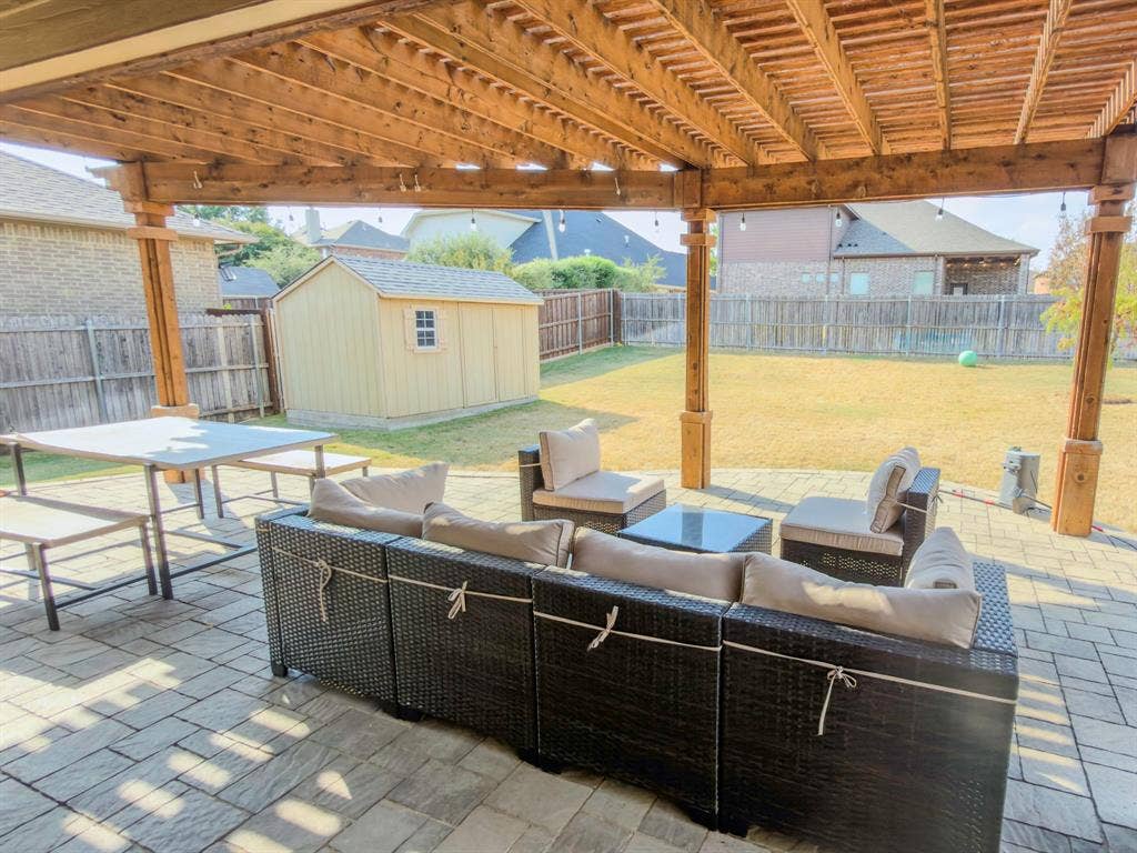 Expansive paver patio with a wood pergola, featuring a large grassy yard and a detached shed structure