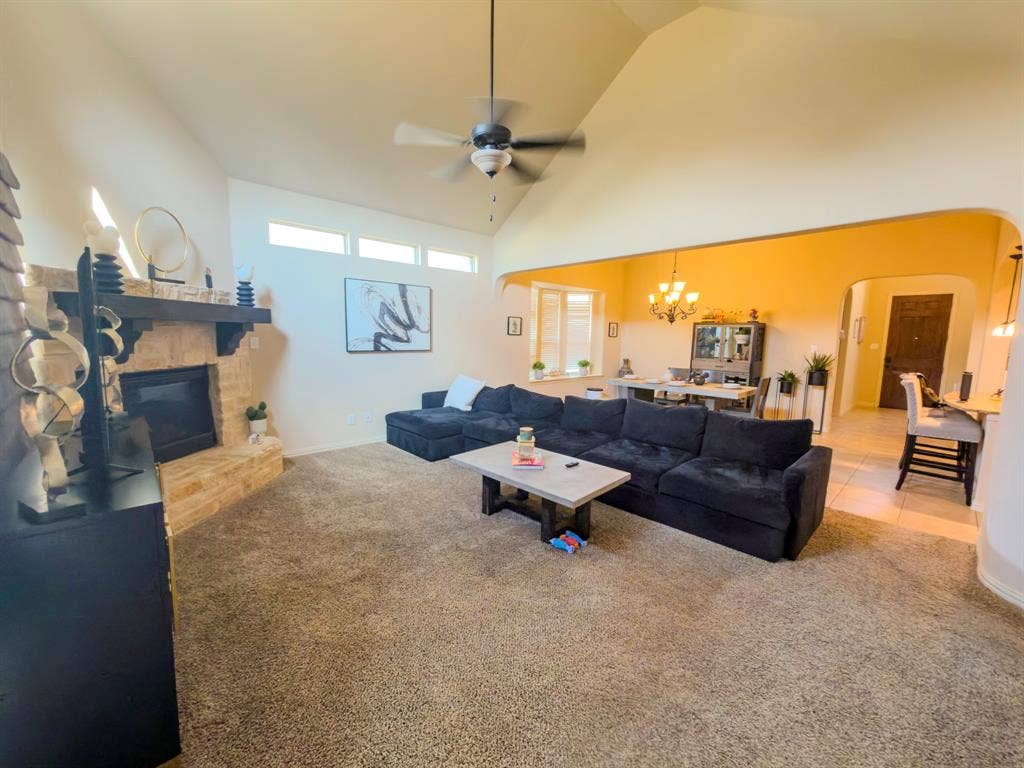 Spacious living area featuring a vaulted ceiling and stone-faced fireplace with a wood mantel