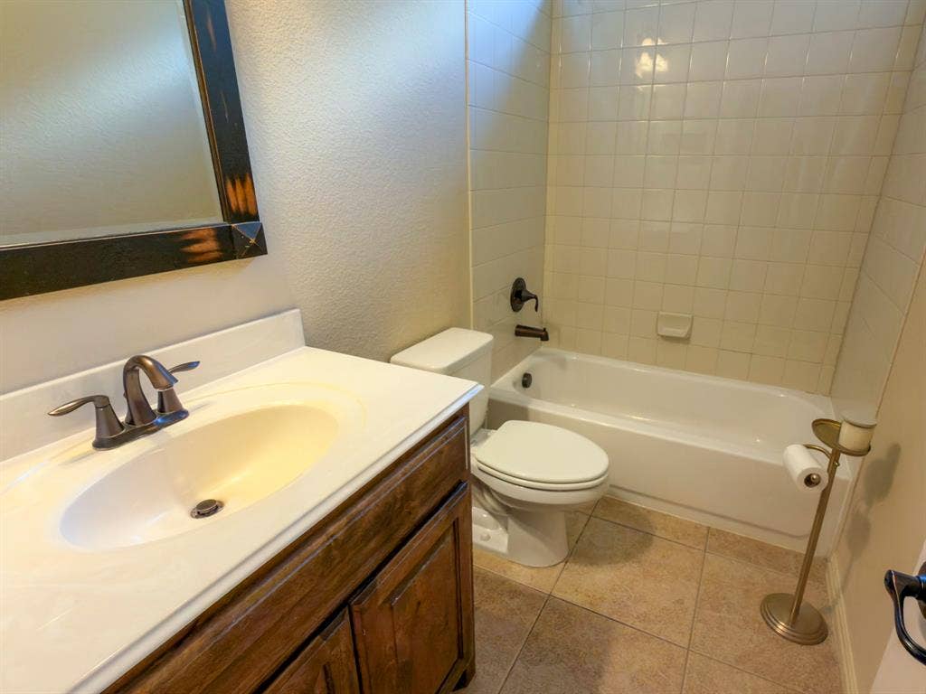 Bathroom featuring a vanity with an integrated sink, a dark wood-finish cabinet, a full-size bathtub, and tiled shower surround