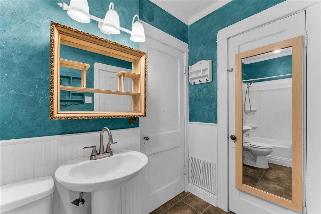 302 W Billington Drive, Robinson, TX 76706 Pedestal sink with brushed nickel faucet, decorative framed mirror, textured wall finish, white wainscoting, and tile flooring