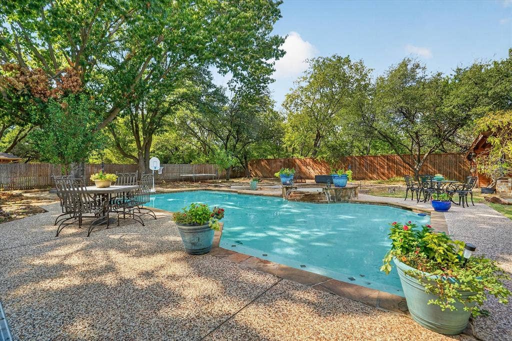7016 Battle Creek Road, Fort Worth, TX 76116 Swimming pool with stone surround, complemented by a private wood fence and mature trees