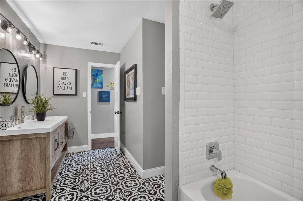 7016 Battle Creek Road, Fort Worth, TX 76116 Bathroom featuring a wood-finish vanity with an integrated sink, patterned floor tile, and a shower-over-tub with white subway tile surround and a rain showerhead
