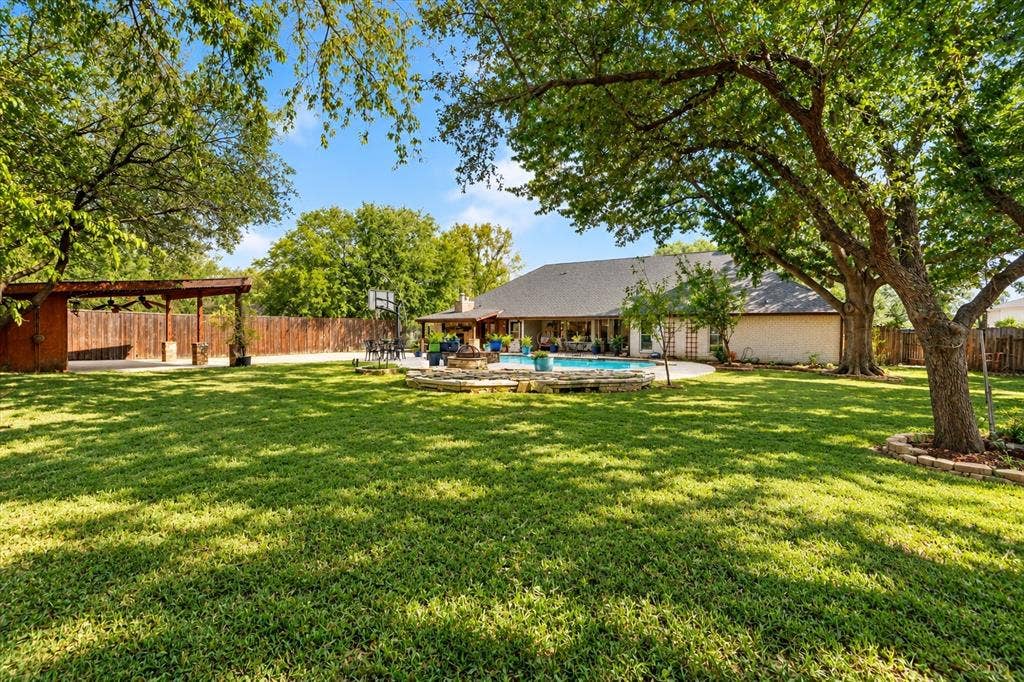 7016 Battle Creek Road, Fort Worth, TX 76116 Expansive backyard featuring a manicured lawn, inground swimming pool, stone fire pit, and a covered patio structure