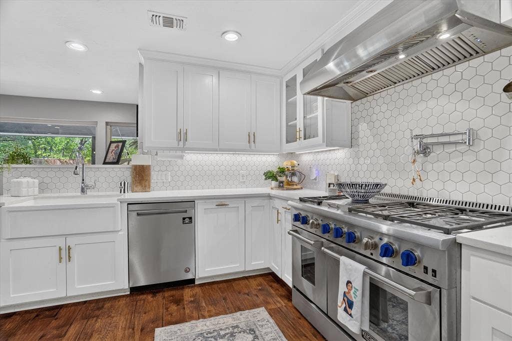 7016 Battle Creek Road, Fort Worth, TX 76116 White shaker cabinetry, honeycomb tile backsplash, stainless steel range with pot filler, farmhouse sink, and wood-finish flooring