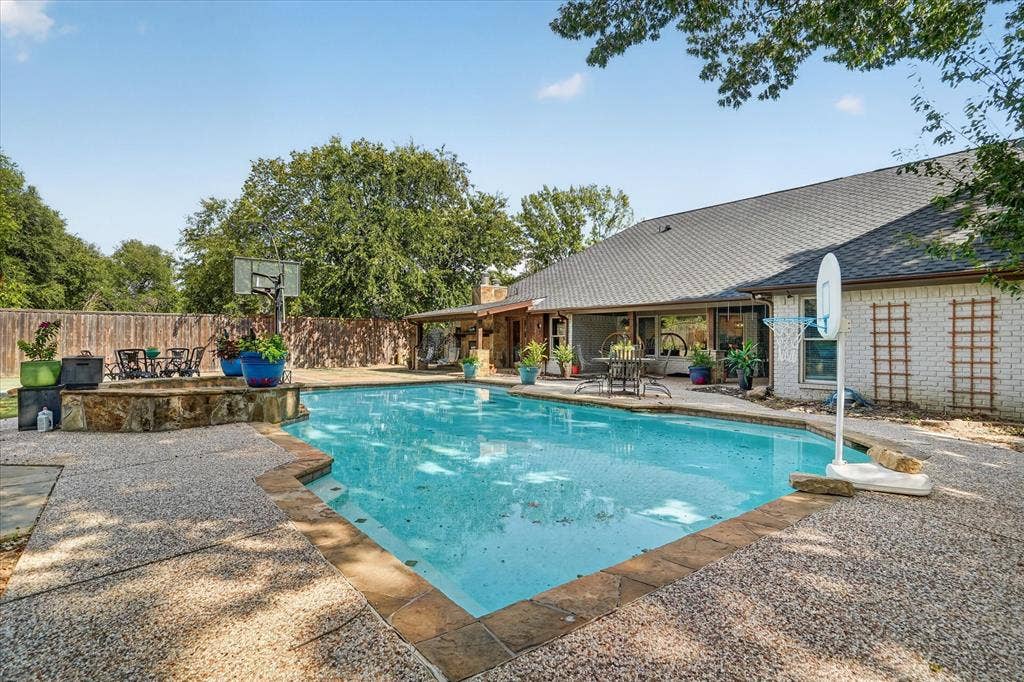 7016 Battle Creek Road, Fort Worth, TX 76116 Expansive outdoor area featuring a swimming pool, textured concrete decking, natural stone accents, and a covered patio